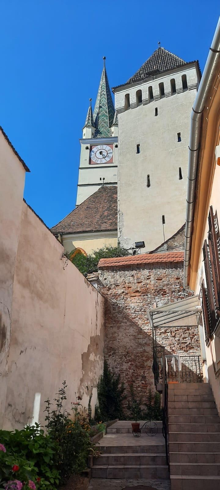 Turnul cu ceas al bisericii fortificate din Mediaș, văzut de pe o stradă în pantă
